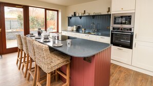 A modern kitchen with a central island, bar stools, a built-in oven, and a view of the outdoors. - Dant Y Llew (Bow Street)