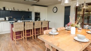 A modern kitchen with a central island, wooden chairs, and a dining table set for six with white tableware. - Dant Y Llew (Bow Street)