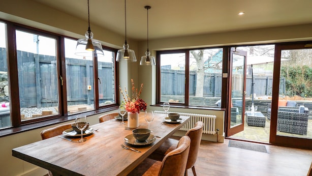 A dining area with a wooden table, chairs, and hanging pendant lights. - Dant Y Llew (Bow Street)