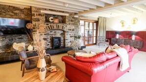 A cozy living room with a stone fireplace, a red leather sofa, and a flat-screen TV mounted above the fireplace. - Dant Y Llew (Bow Street)