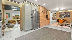 A modern kitchen with a stainless steel refrigerator, wooden wall paneling, and a dining area with orange chairs. - Chic Newberg Oasis: Mid-Century, Hot Tub, Fire Pits, Luxury Amenities (Newberg)