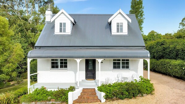 A two-story house with a grey roof, white exterior walls, and a front porch with steps leading to the entrance.