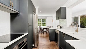 Una cocina moderna con armarios oscuros, encimeras blancas y un comedor con sillas de madera.