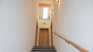 A narrow staircase with a wooden door at the top, a handrail on the right, and a small window at the top.