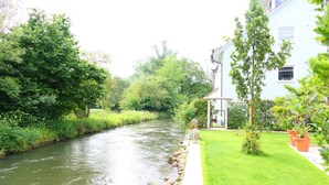 A river flowing alongside a building with a well-maintained lawn and potted plants.