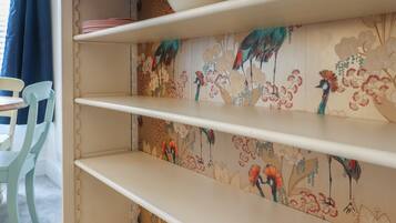 A kitchen with a decorative backsplash featuring a bird and floral pattern, white shelves, and a blue chair.