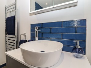 A modern bathroom with a white sink, a blue tiled backsplash, and a towel rack.