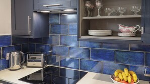 A kitchen with dark blue cabinets, a built-in microwave, a toaster, and a bowl of fruit on the counter. - Sally (Whitstable)
