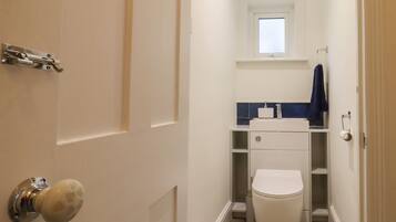 Une petite salle de bain étroite, avec des toilettes, un lavabo et une fenêtre.