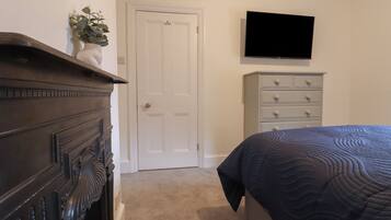 Een slaapkamer met een donker houten dressoir, een witte deur, een grijze dressoir en een bed met een donkere quilt.