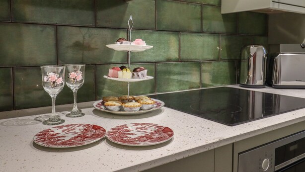 Eine Küchenarbeitsplatte mit einem dreistöckigen Cakestand, zwei Gläsern und zwei Tellern mit roten Mustern.