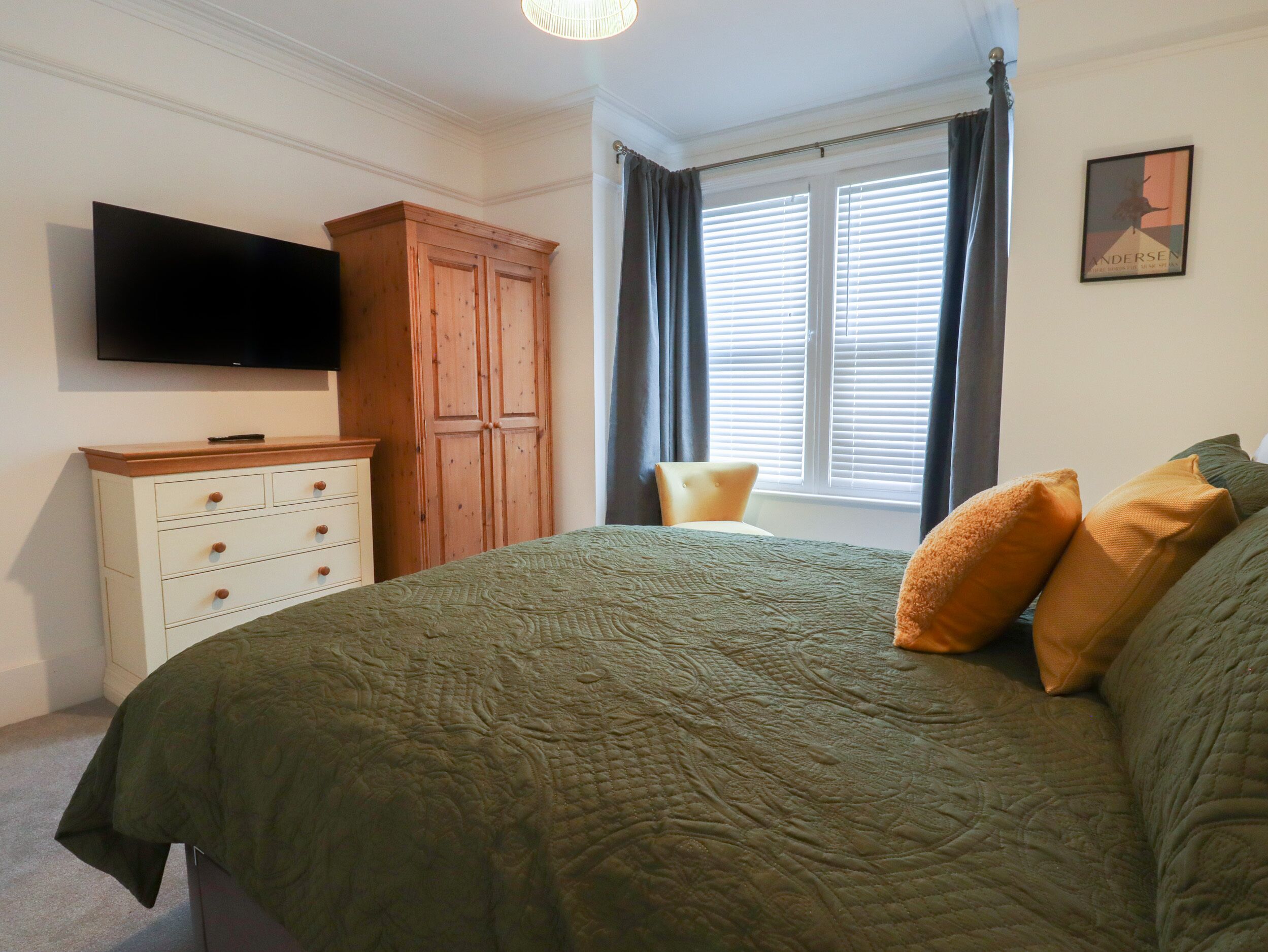 A bedroom with a bed, a dresser, a television, a window with curtains, and a framed picture on the wall.
