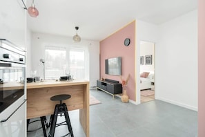 A modern kitchen with a wooden countertop, a bar stool, and a dining area with a white sofa and a TV.