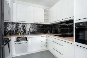 A modern kitchen with white cabinets, a black backsplash, and a built-in oven.