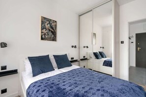 A bedroom with a bed, a large mirror, a wall-mounted artwork, and a door with a keyhole.