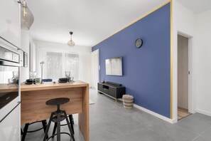 A modern kitchen with a wooden countertop, a bar stool, and a dining area with a blue accent wall.