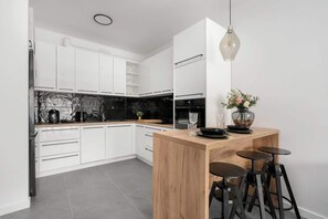 A modern kitchen with white cabinets, a wooden island with stools, and a hanging light fixture.