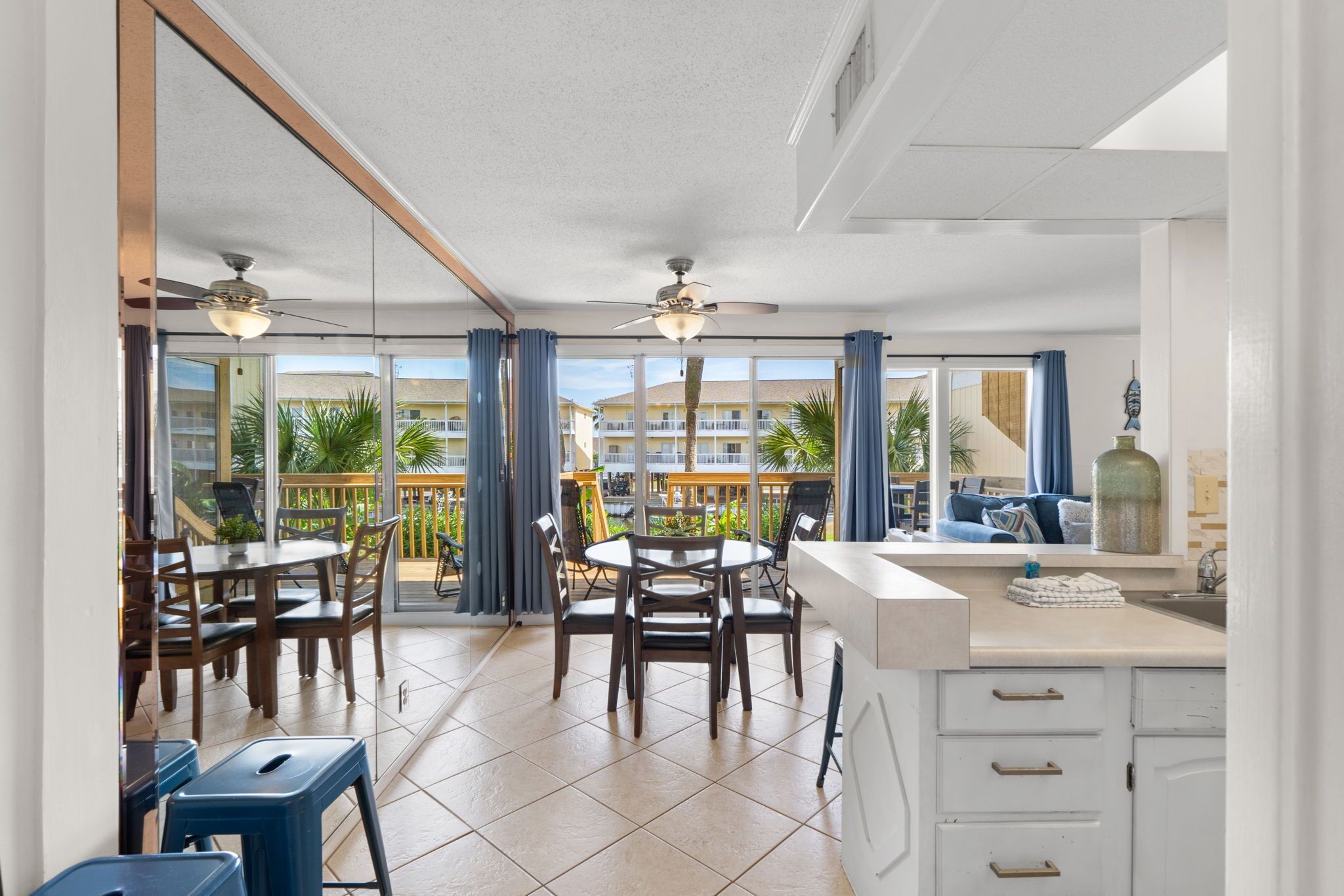 A modern kitchen with a dining area, large windows, and a balcony with a view of other buildings.