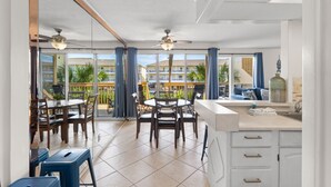 A modern kitchen with a dining area, large windows, and a balcony with a view of other buildings. - Destin 1BR Canal Condo on Golf Course (Destin)