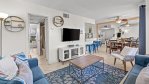 A modern living room with a TV, sofa, coffee table, and dining area with chairs and a table. - Destin 1BR Canal Condo on Golf Course (Destin)