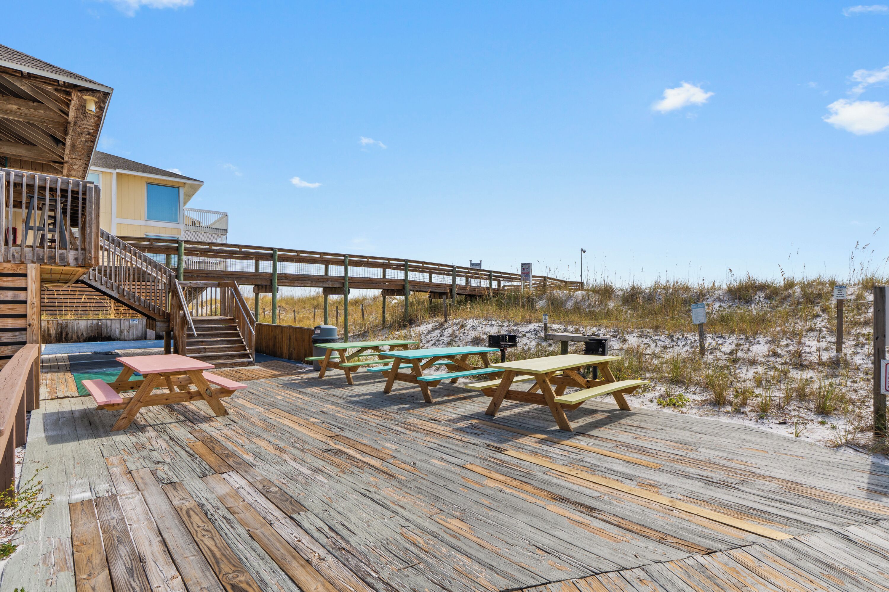 A wooden deck with picnic tables and a staircase leading to a building with a balcony.