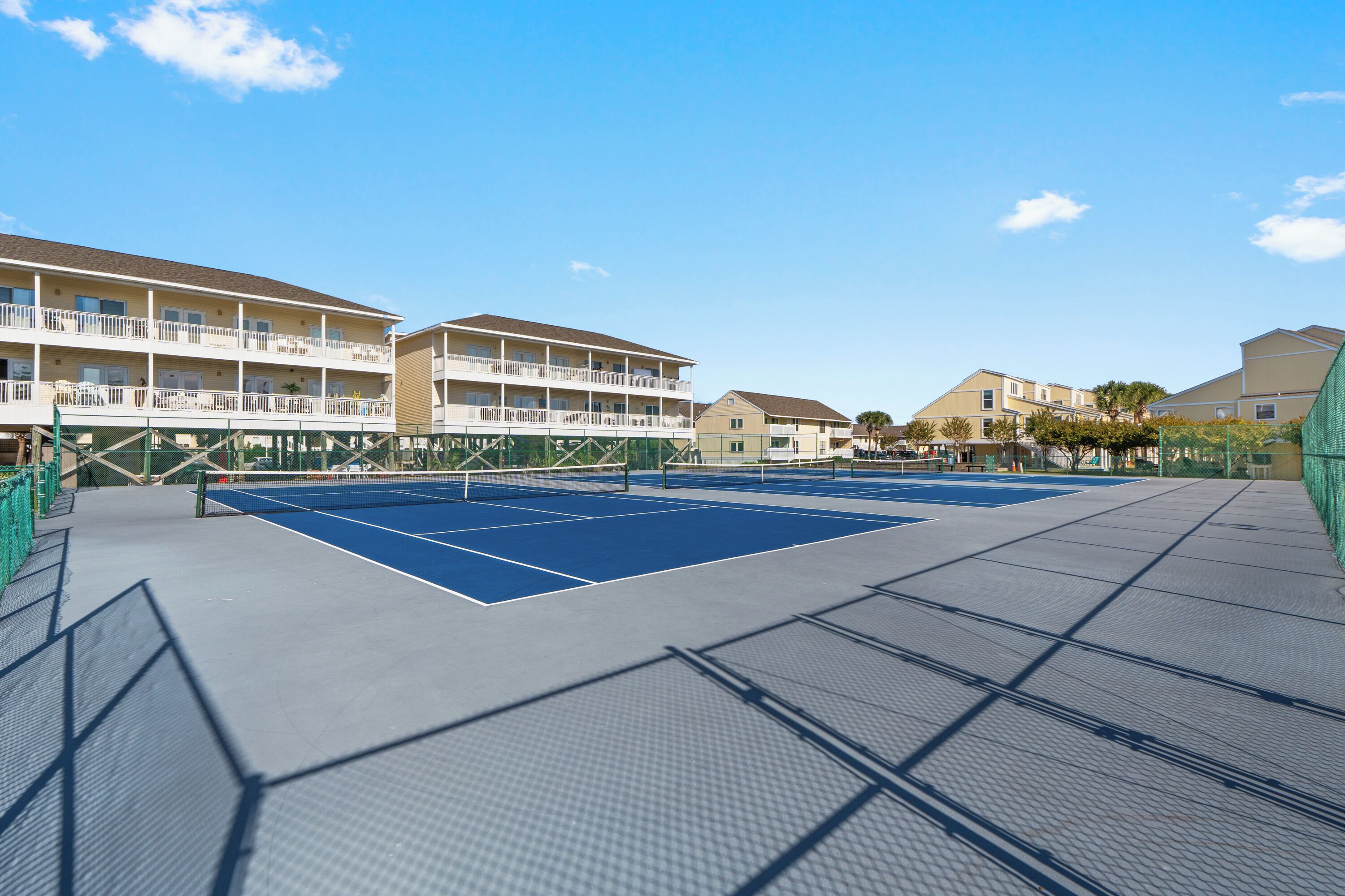 Un court de tennis en plein air, équipé d’un filet, entouré d’immeubles dotés de balcons.