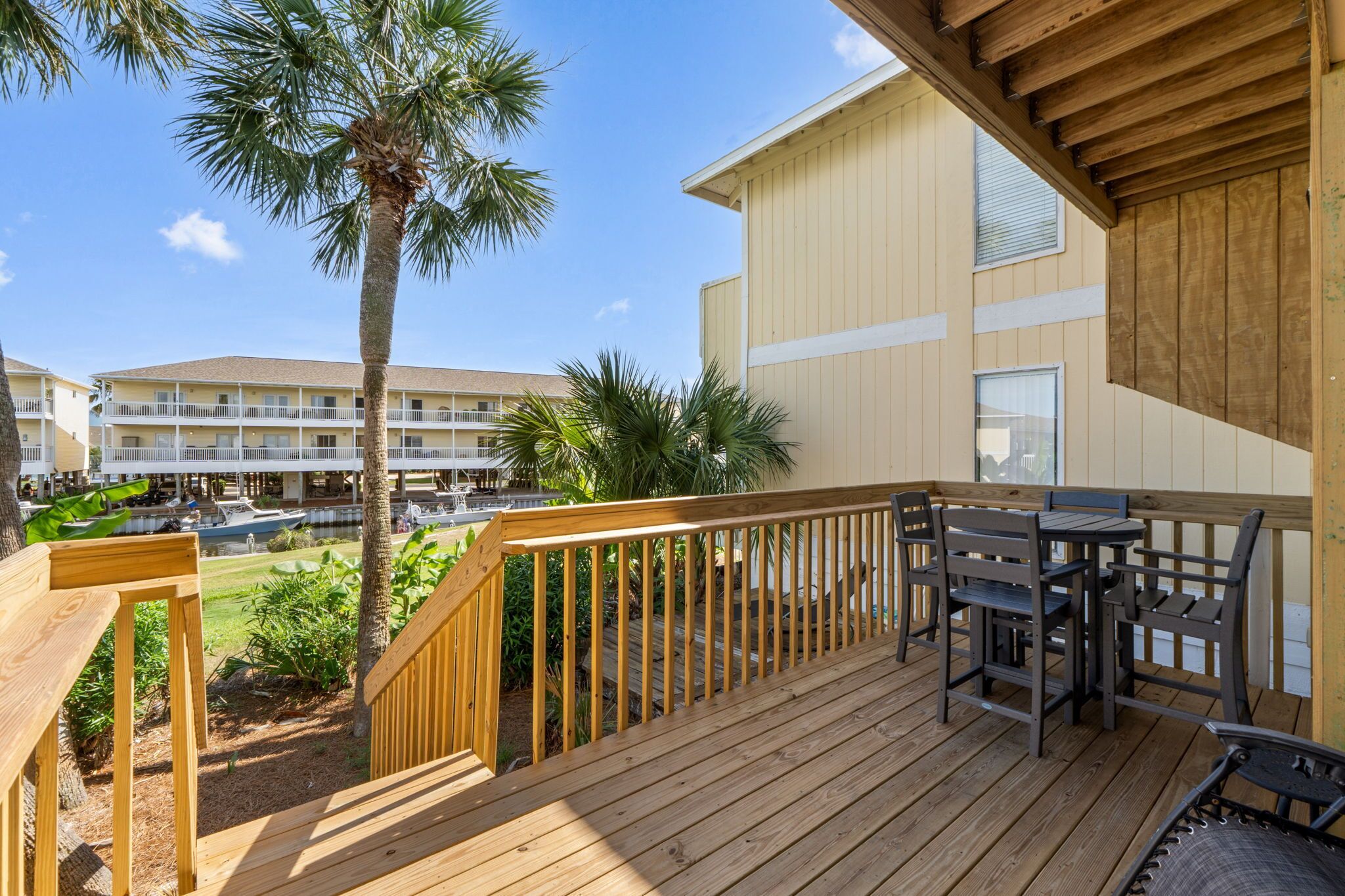 A wooden deck with outdoor furniture, a palm tree, and a view of a hotel building with multiple balconies.