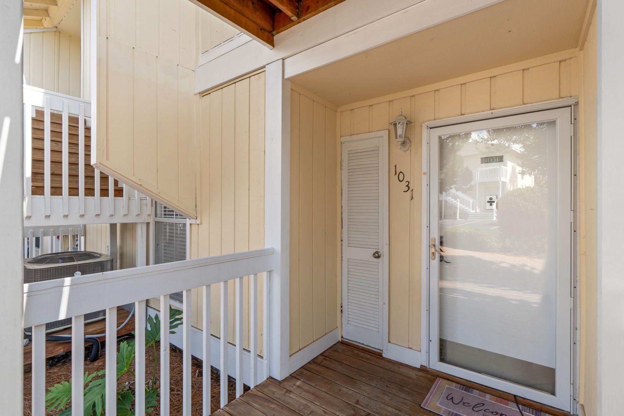 A wooden porch with a white door marked '1031,' a small outdoor seating area, and a white railing.