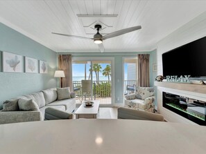 Step into your serene coastal retreat where calming sea-foam walls and plush seating invite you to unwind. Through the balcony doors, palm trees frame your private view of sparkling turquoise waters and soft sand—your perfect escape awaits. - Bayfront Condo: Resort & Views (Tampa)