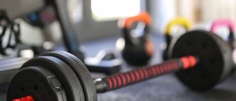 Un gimnasio con equipo de ejercicio, incluyendo mancuernas, balones de pesa y una bicicleta estática.