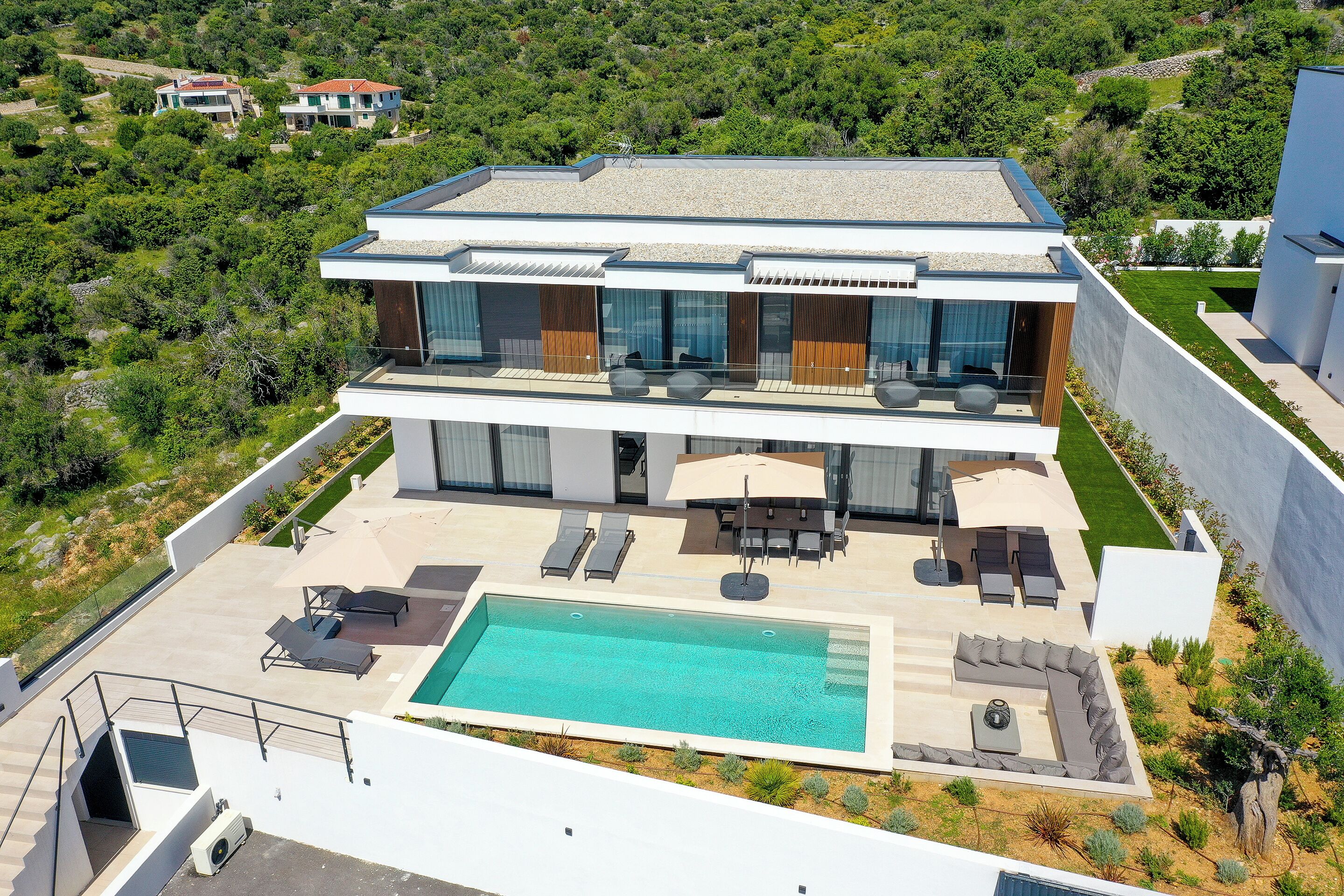 Et moderne hus med to etager, en swimmingpool, udendørs siddepladser og udsigt til det grønne omkring.