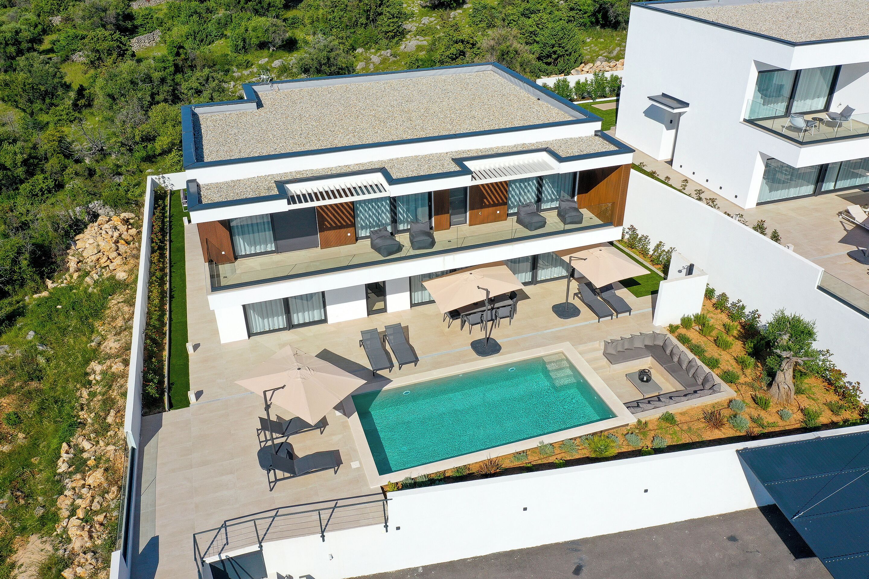 A modern two-story house with a swimming pool, outdoor seating, and a view of the surrounding landscape.