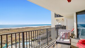 A balcony with a view of the beach and ocean. There is a pool, lounge chairs, and a red chair. - Beachfront 3BR, Pools, Hot Tubs, New to Rentals!! (Orange Beach)