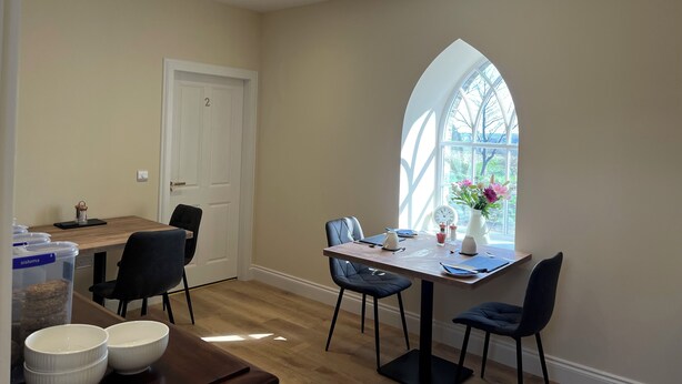 A dining area with a wooden table, black chairs, and a window with a view of greenery. - Grainbank Mews (Kirkwall)