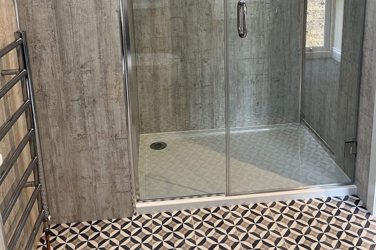 A modern shower area with glass doors, a metal handrail, and a patterned floor.