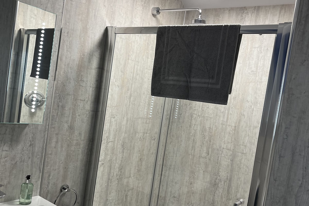 A modern bathroom with a glass-enclosed shower, a white sink, and a mirror with lights.