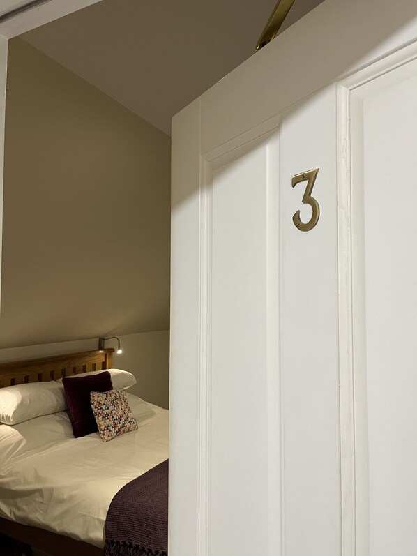 A hotel room with a bed, a nightstand, and a door with the number 3. - Grainbank Mews (Kirkwall)