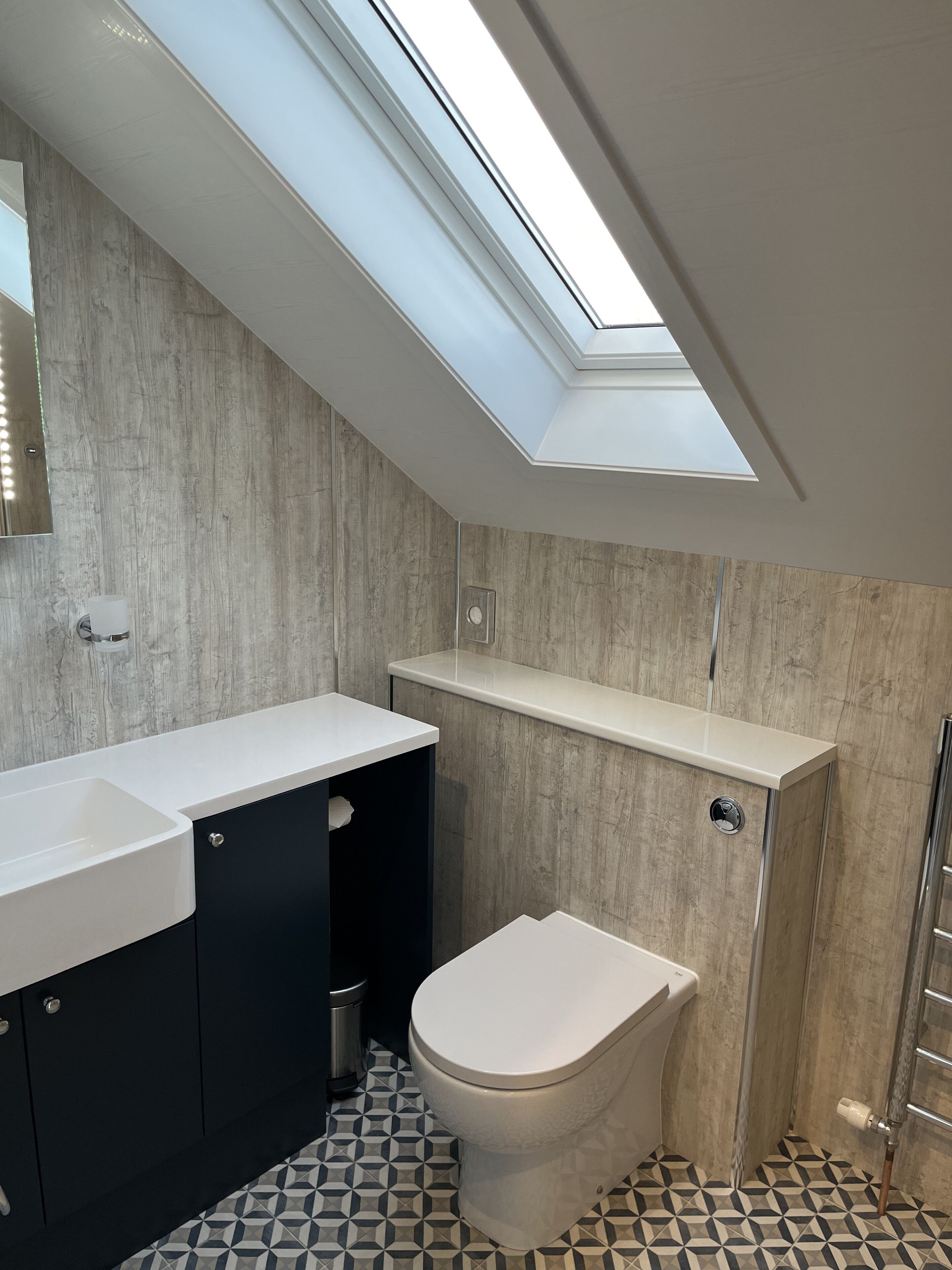 Un baño moderno con tragaluz, inodoro blanco, mueble negro y lavabo blanco.
