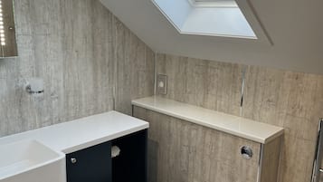 Un baño moderno con tragaluz, inodoro blanco, mueble negro y lavabo blanco.