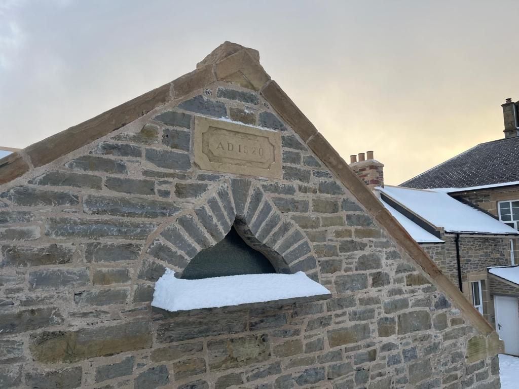 Edifício de pedra com placa comemorativa, ano 1820, e entrada coberta de neve.