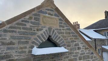 Edifício de pedra com placa comemorativa, ano 1820, e entrada coberta de neve.