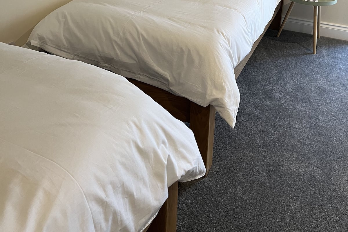 A single bed with white bedding in a room with a sloped ceiling and a small round table with a clock.