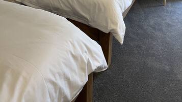Una cama individual con ropa de cama blanca en una habitación con techo inclinado y una pequeña mesa redonda con un reloj.
