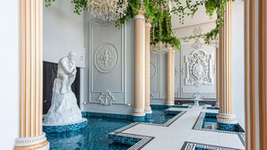 Un área de piscina interior lujosa con columnas ornamentales, una estatua de mármol y paneles decorativos en las paredes.
