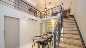 Un comedor con una mesa preparada para cuatro personas, una escalera y un equipo de aire acondicionado en la pared.