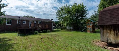 A backyard with a wooden deck, a brick house, and a play structure.