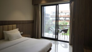A modern hotel room with a large bed, a view of the outdoor balcony, and a sliding glass door. - Mansa Club And Resort (Ujjain)