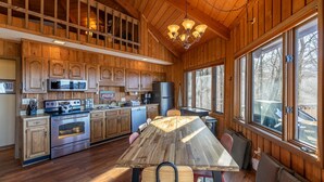 Une cuisine spacieuse avec des meubles en bois, une grande table à manger et une vue sur l’extérieur grâce à de grandes fenêtres.