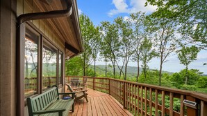 Une terrasse en bois avec un banc et une table, offrant une vue sur un paysage boisé.