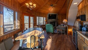 L’intérieur d’un chalet en bois comprend une table à manger, des chaises, une cheminée, un téléviseur et un coin cuisine.